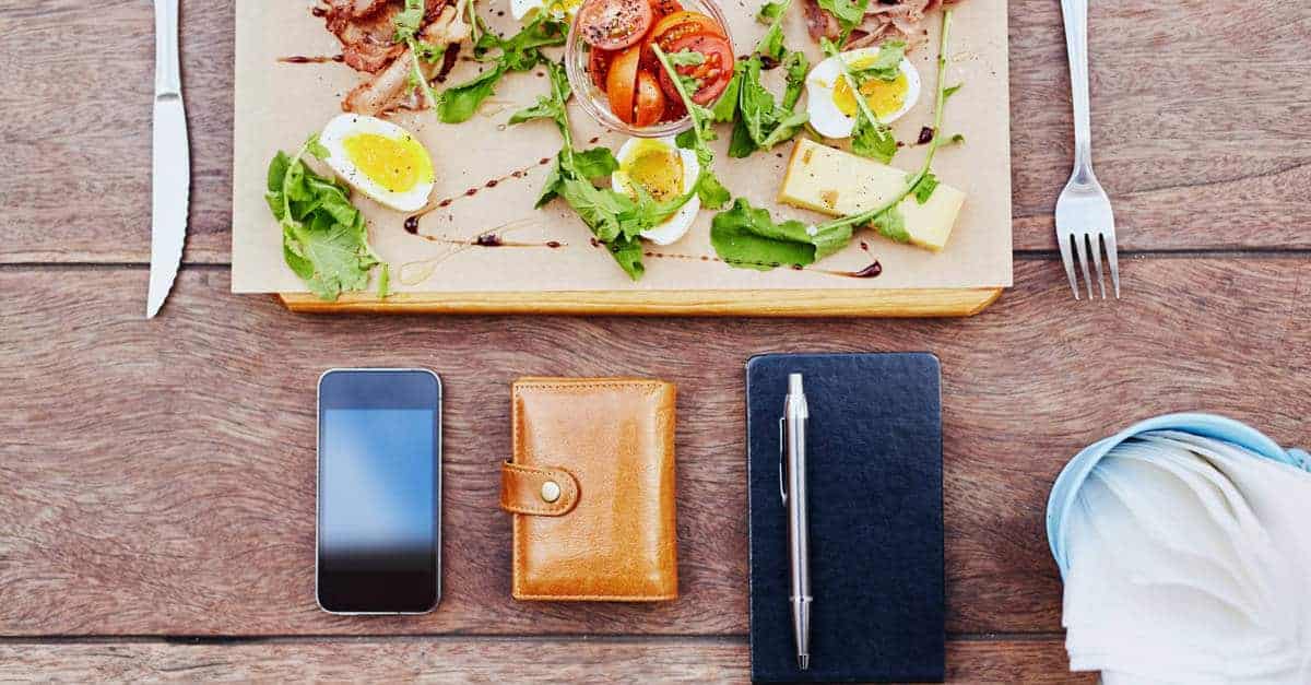 Wooden board with salad on it aligned with a smartphone, wallet and notebook