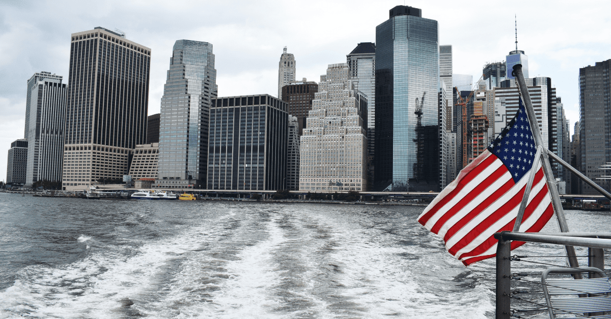 The city skyline viewed from a ferry with an American flag in the foreground.