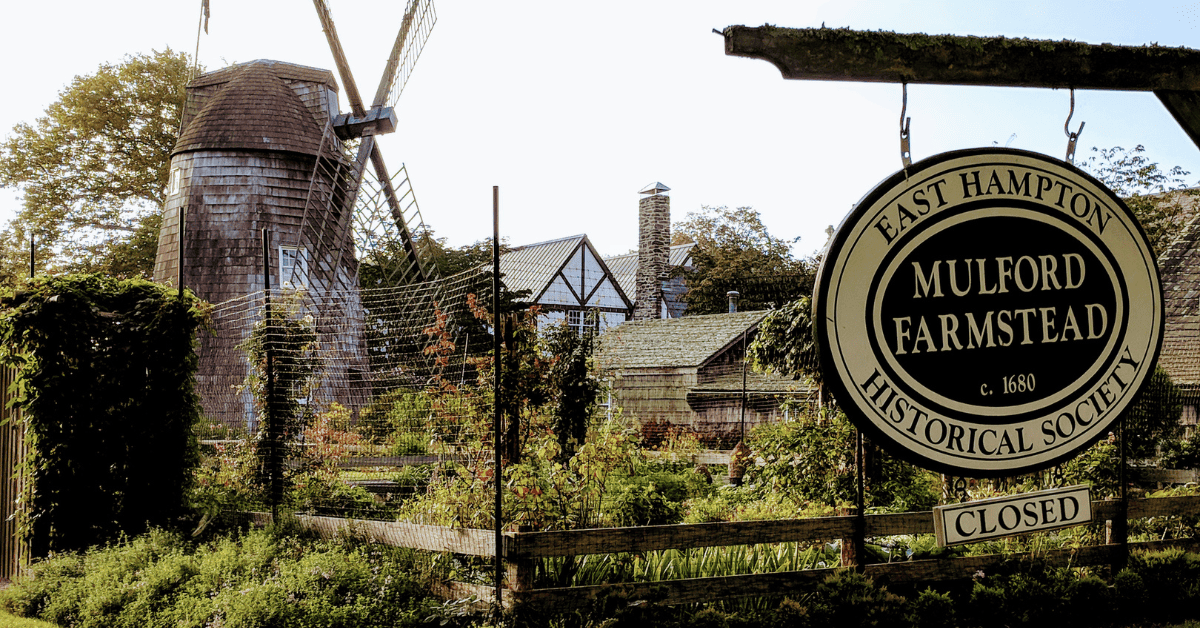 a sign for a farm with a windmill in the background.
