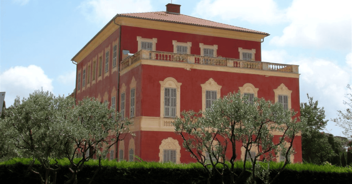 a large red building with a balcony and trees in front of it.
