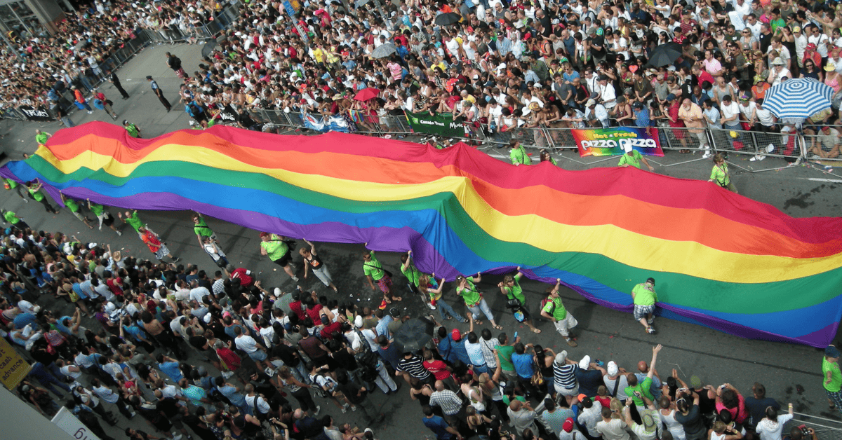 a large rainbow flag being carried down a street.