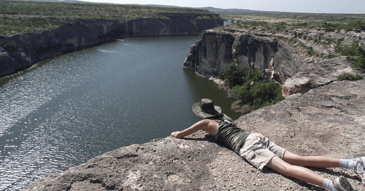A man is laying on a cliff overlooking a river.