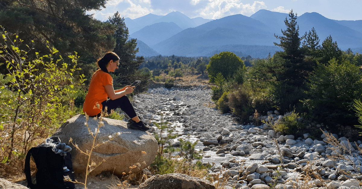 A woman sits on a rock and looks at her phone.