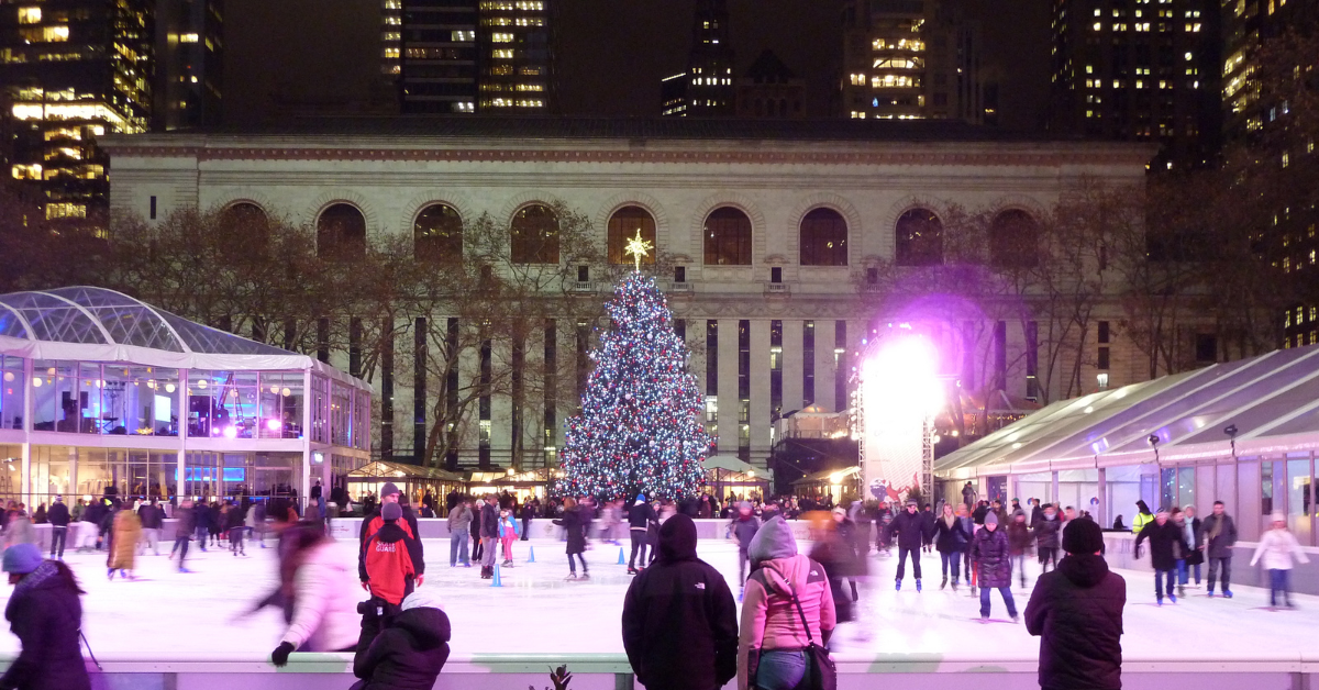 An outdoor ice skating rink with a large Christmas tree and a historical building in the night.