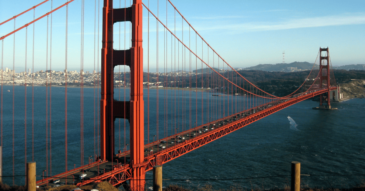 A panoramic view of the iconic Golden Gate Bridge in San Francisco, with cars traveling on it, set against a backdrop of the cityscape and clear blue skies.
