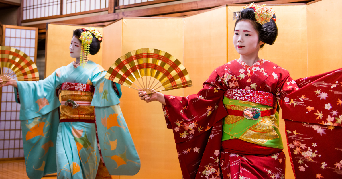 Two individuals in traditional Japanese attire holding decorative fans, with their faces obscured for privacy.