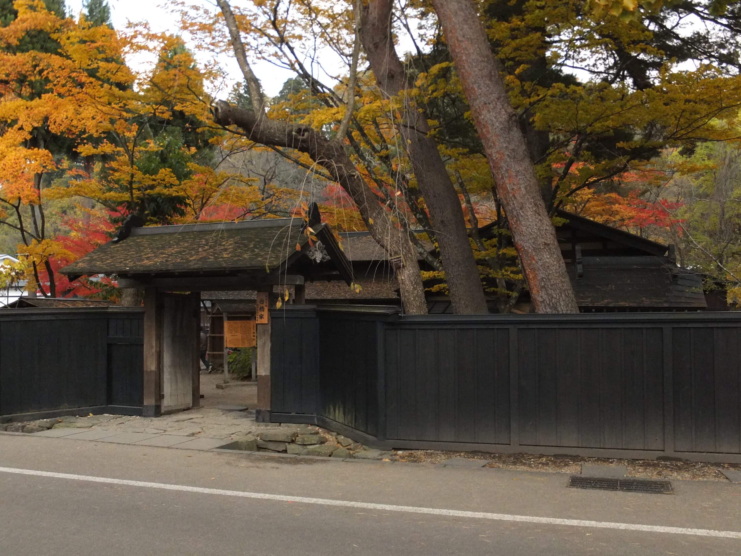 A serene autumn scene featuring a traditional wooden gate and fence in front of a house.
