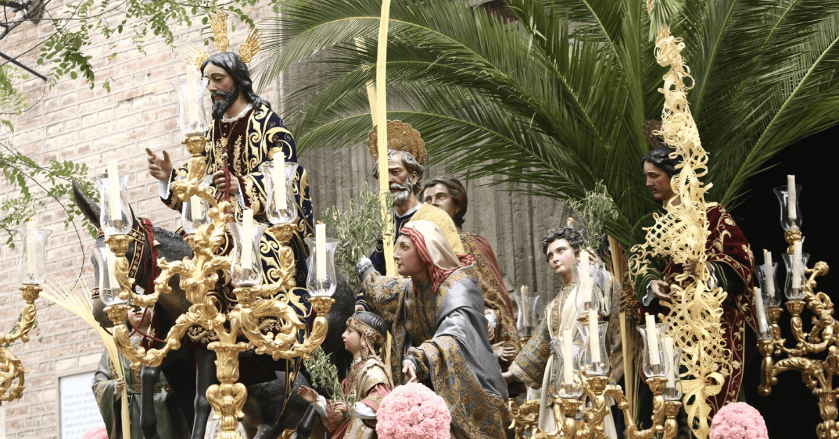 A golden float adorned with figures and flowers moves solemnly through ancient streets during Semana Santa.