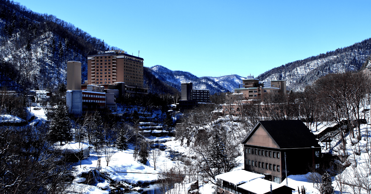 A snowy landscape with buildings nestled between snow-covered mountains under a clear blue sky.