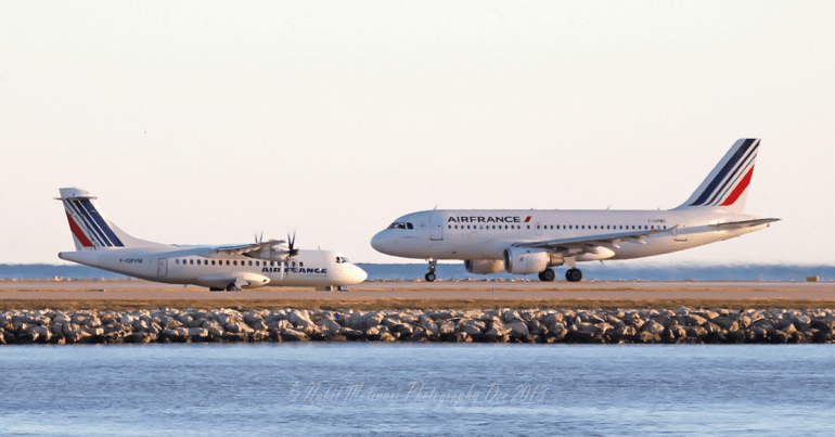 Two Air France aircrafts, a smaller propeller plane and a larger jet, are parked on the tarmac near a body of water during daylight.