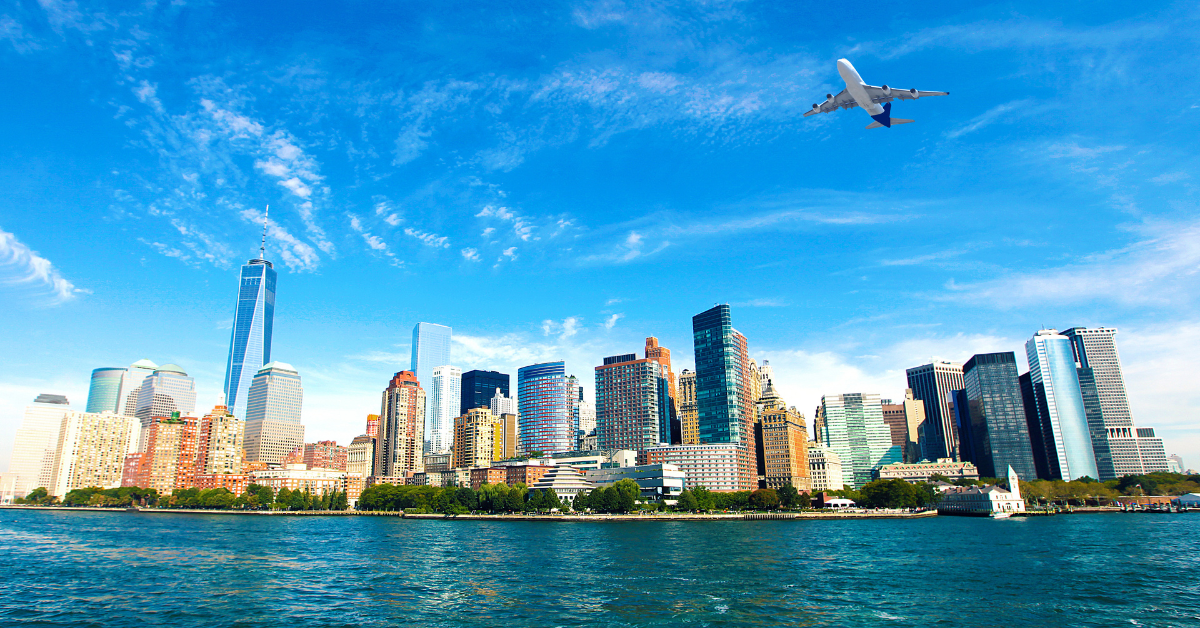 A plane soaring above a city skyline against a clear blue sky.