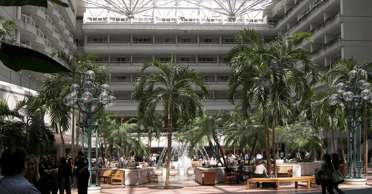 A crowded indoor space with numerous individuals and palm trees.