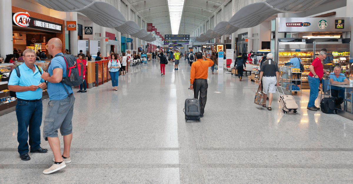 People walking in a busy airport terminal, carrying luggage and wearing various outfits.